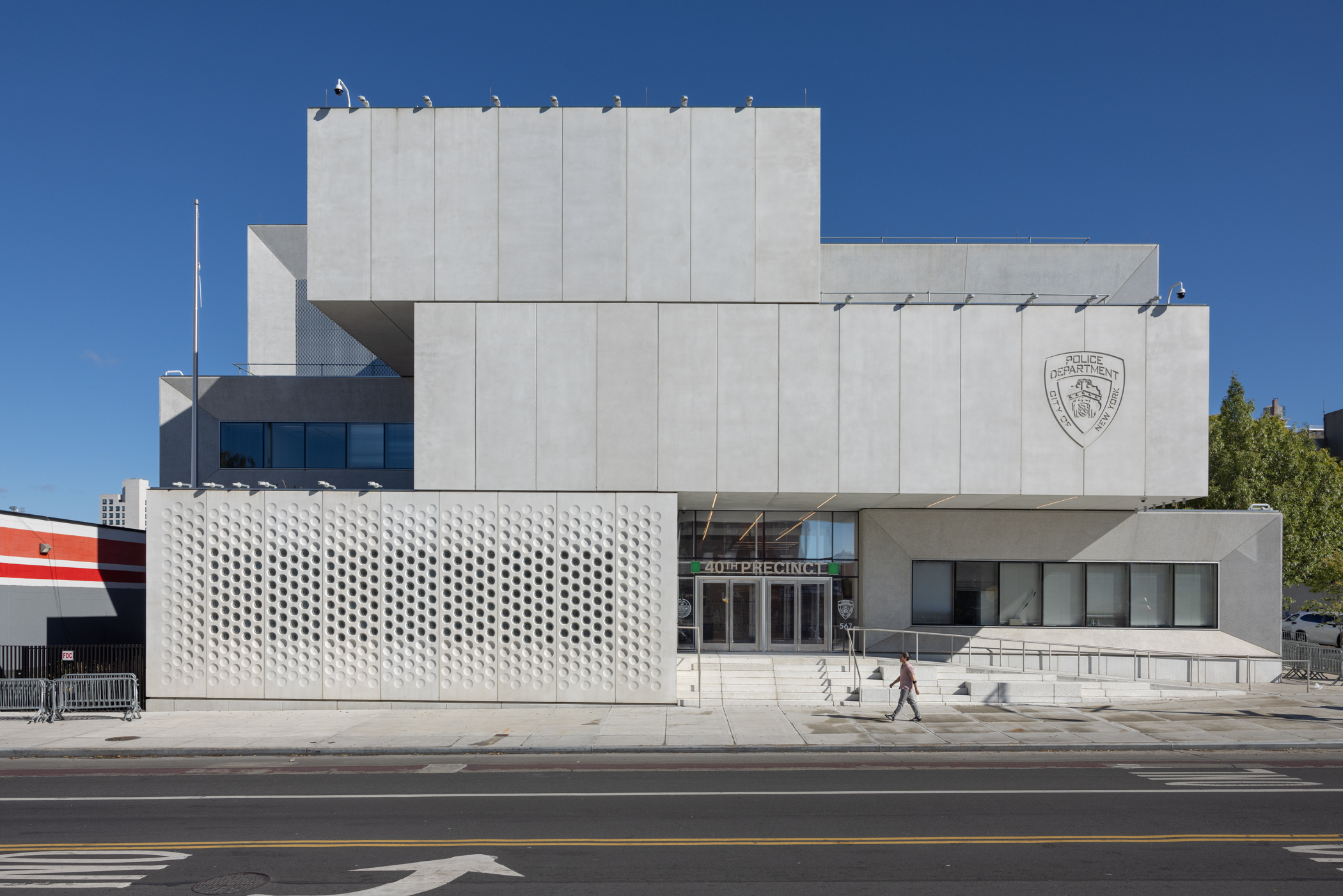 Exterior of a building that looks like three concrete rectangles stacked on top of each other asymmetrically. The ground floor has windows on the right side and a circular perforated facade on the left.