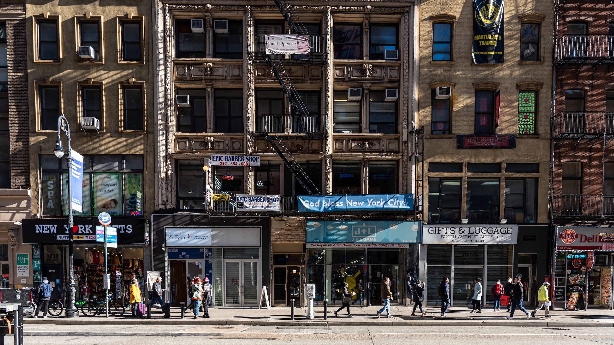 A wide shot of a Manhattan street showing the sidewalk and several stories of a city block including retail spaces.