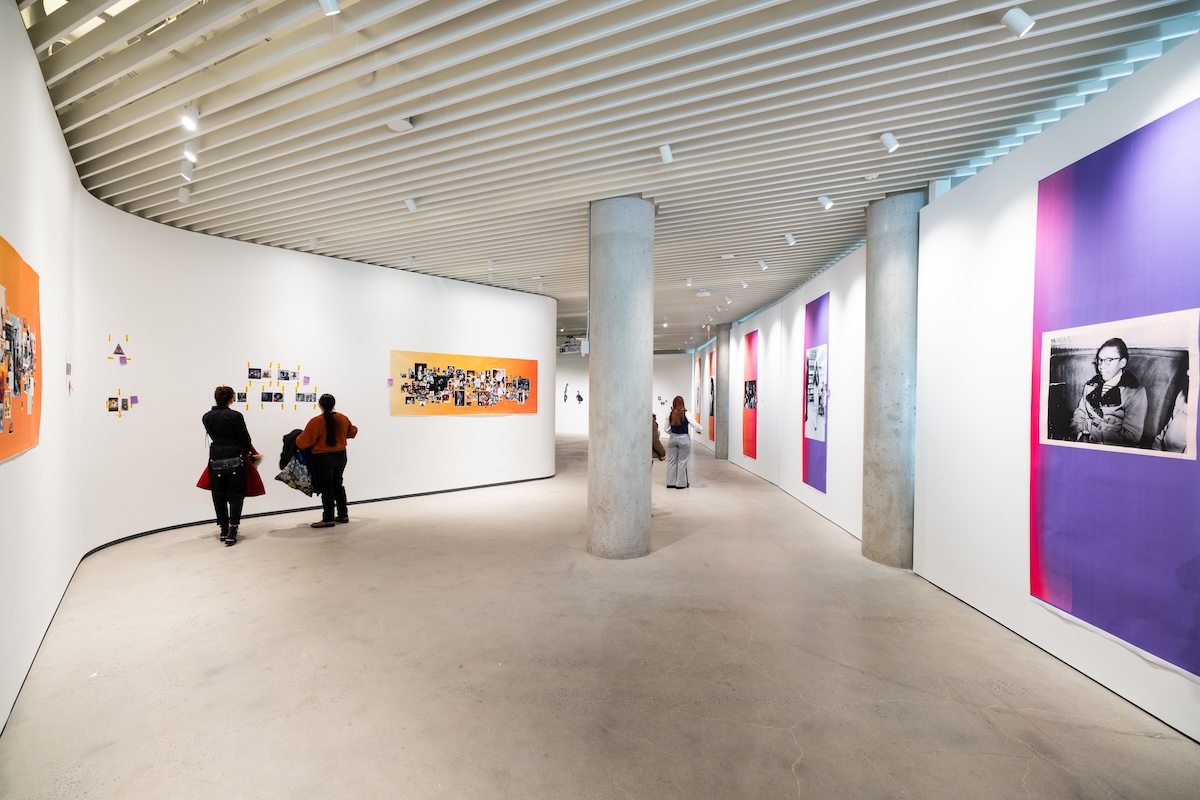 Four people stand inside of an industrial-like gallery space with several photo installations on white gallery walls.