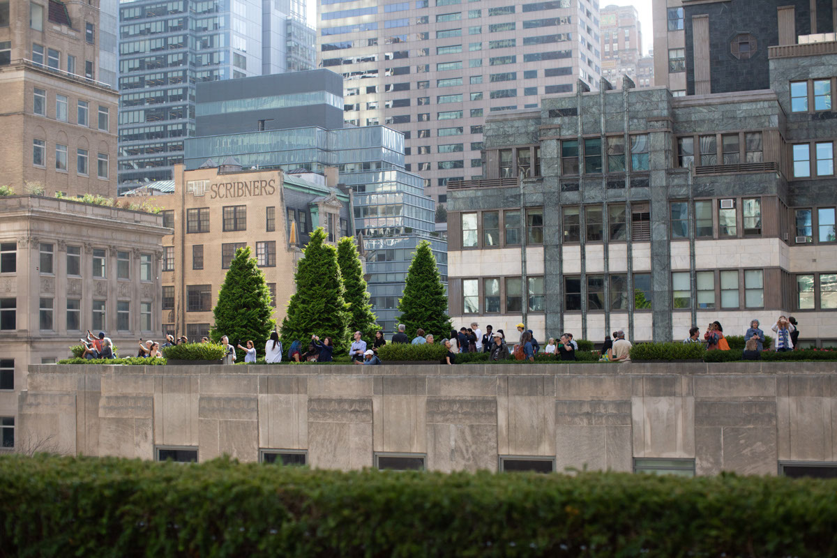 A rooftop garden filled with people in midtown Manhattan, with skyscrapers surrounding it.