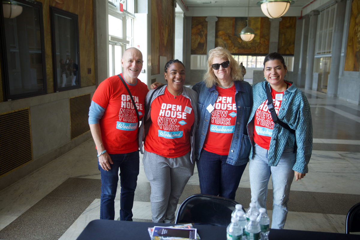 Four people in matching red Open House New York shirts smiling and posing together indoors.