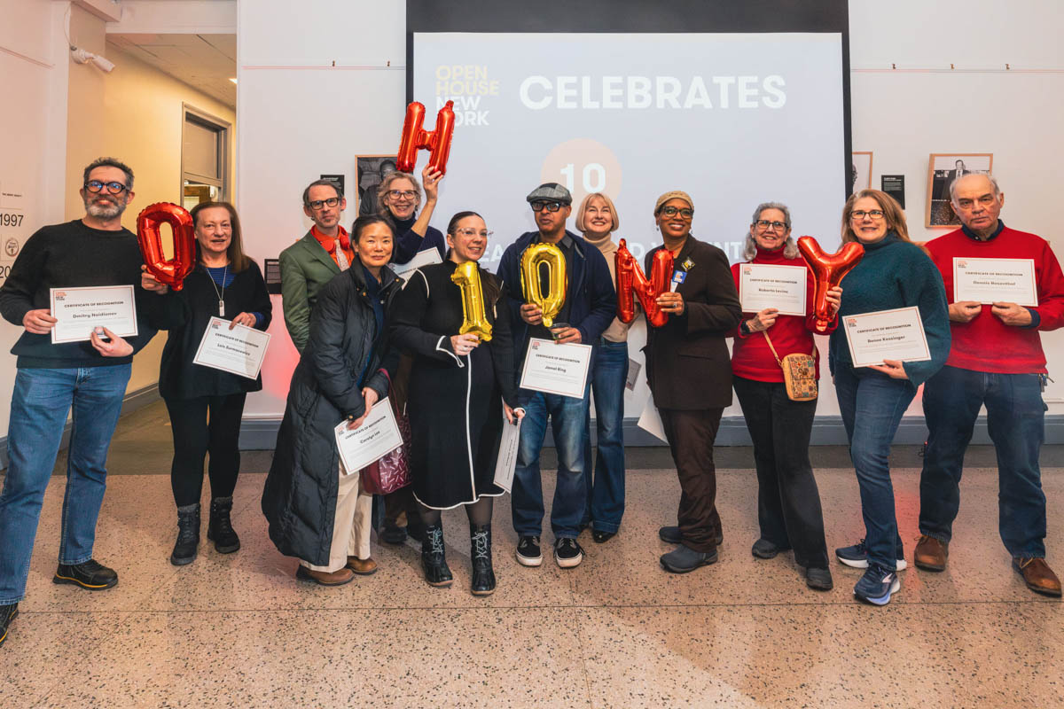 Twelve people hold certificates and balloon letters spelling OHNY, standing together in a brightly lit room.
