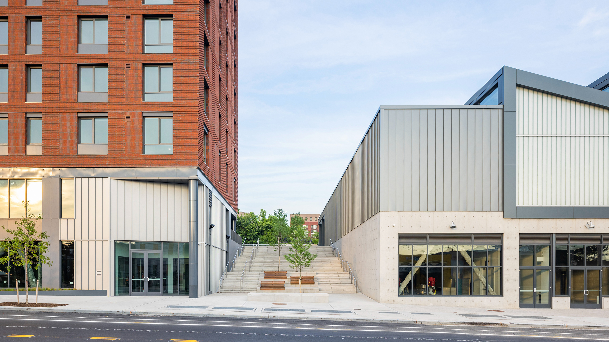 A red brick building and a modern gray building with stairs between them on a city street.