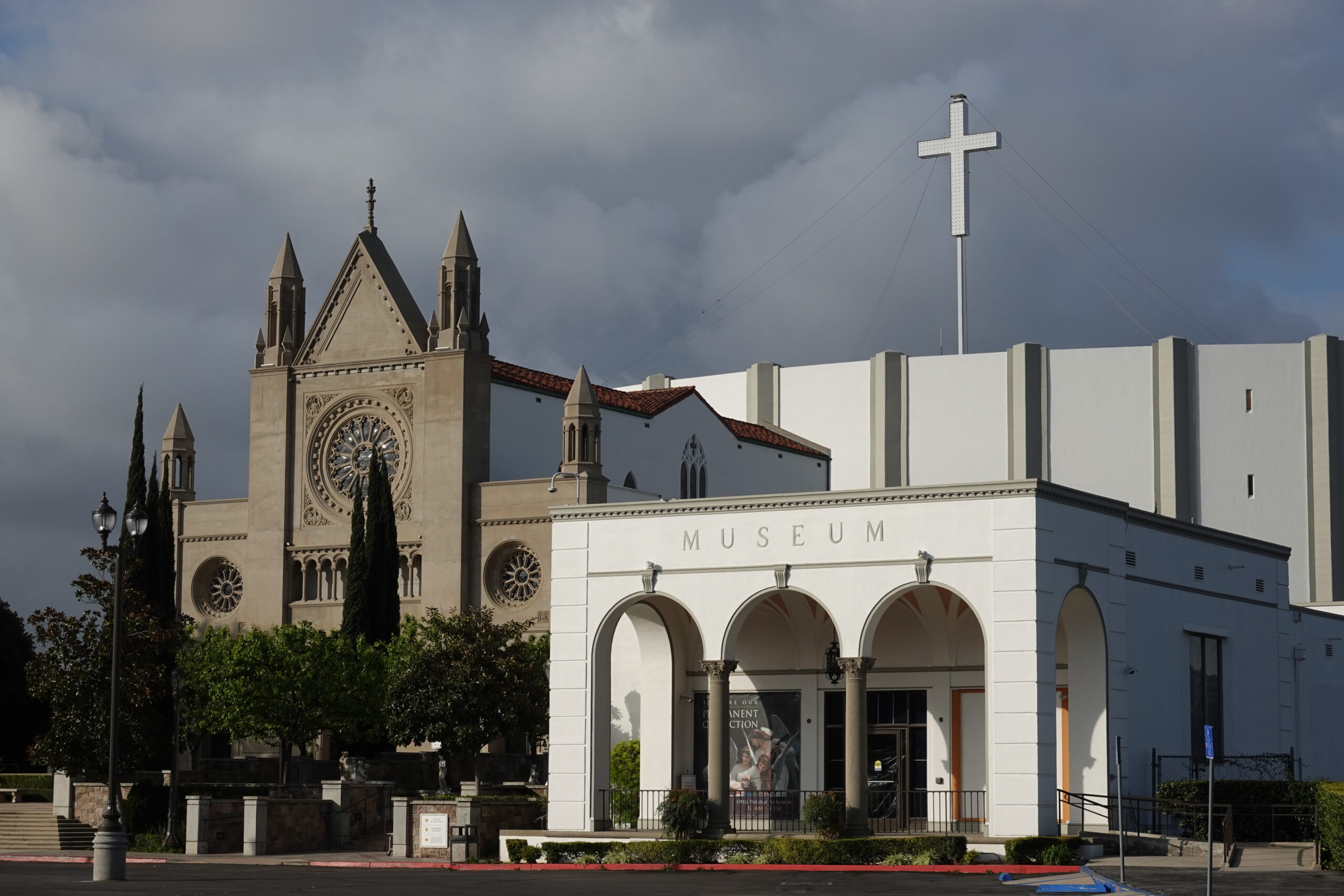 Museum building with arched entry in front of a large church with a cross and stained glass window.
