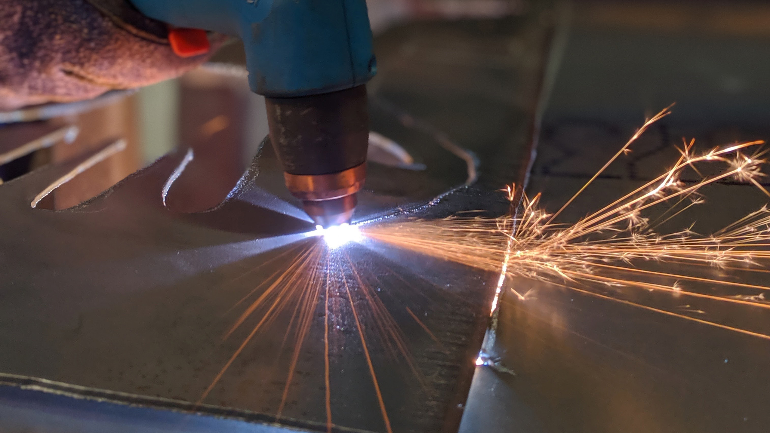 Close-up of a plasma cutter slicing through metal, with bright sparks flying to the right.