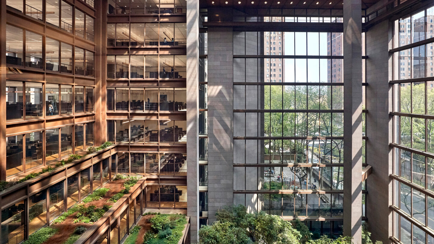 Large open office building with glass walls, indoor greenery, and views of trees and city buildings outside.