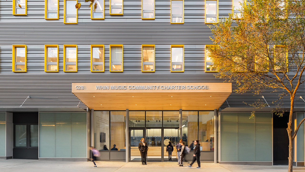 People stand outside the entrance of a modern building labeled WINN MUSIC COMMUNITY CHARTER SCHOOL.