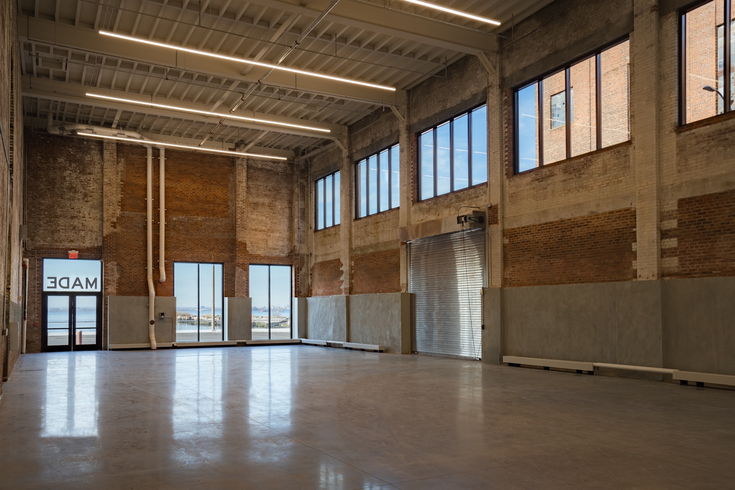 Spacious industrial-style room with large windows, exposed brick walls, and polished concrete floors.
