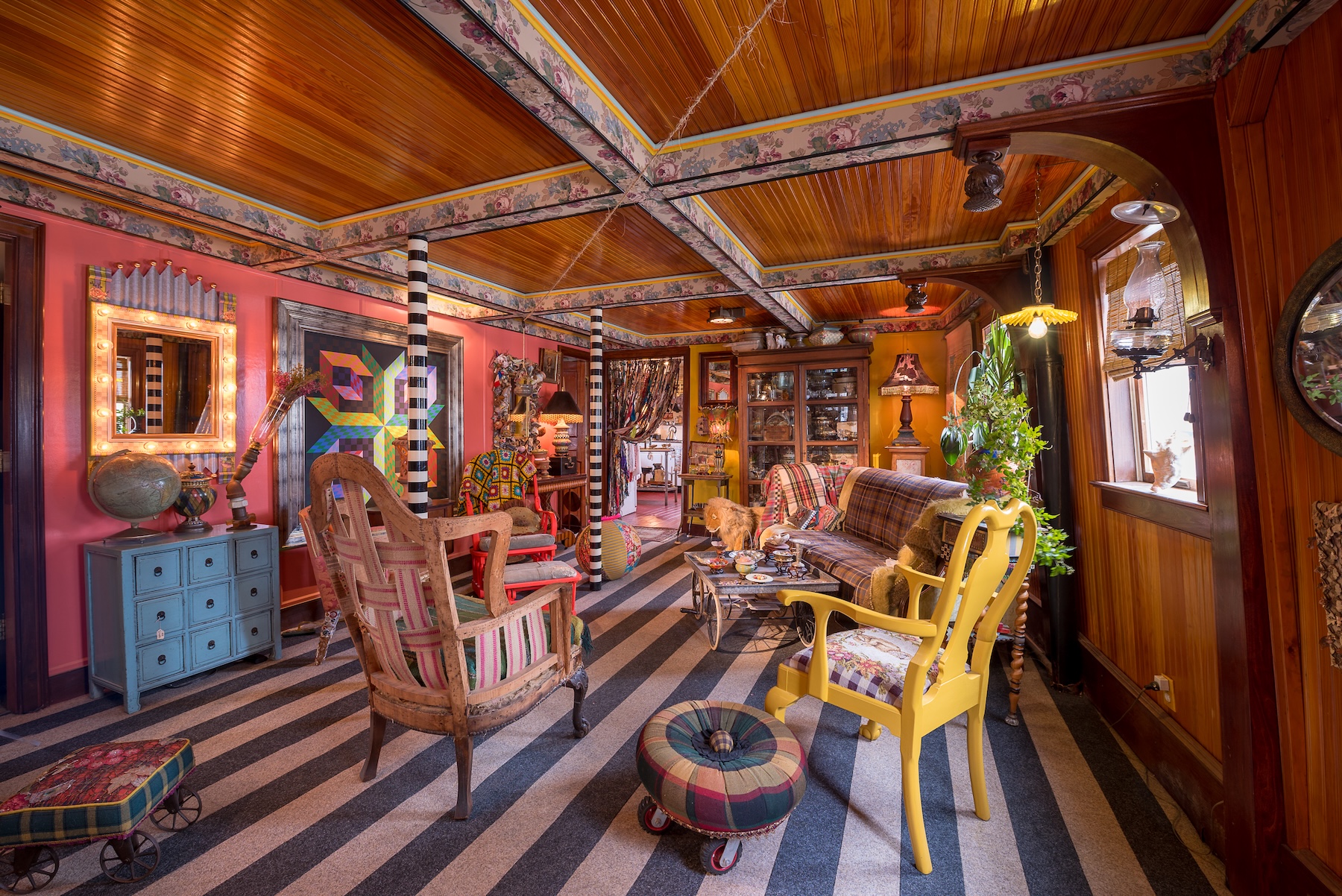 Eclectic living room with bold colors, striped floor, mismatched furniture, and vibrant decor accents.