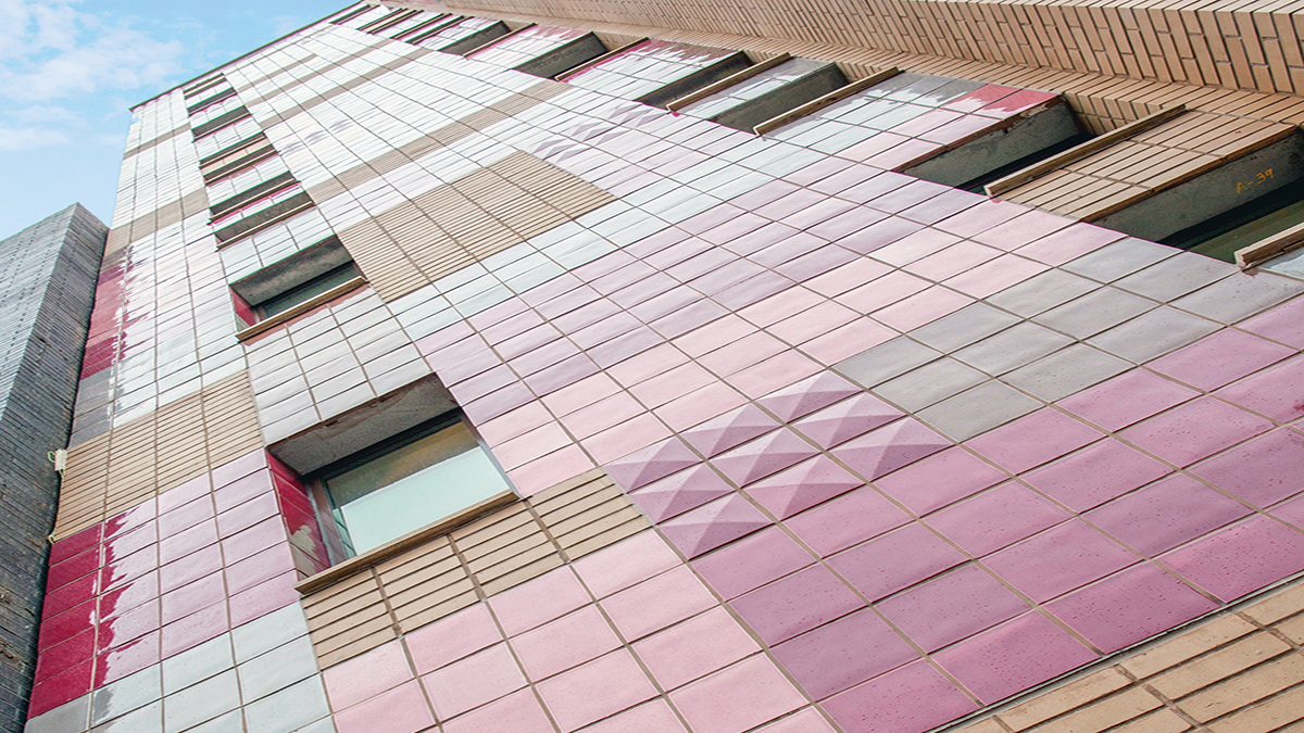 Tall building with pink and beige tiles, viewed from below, with geometric patterns and windows.