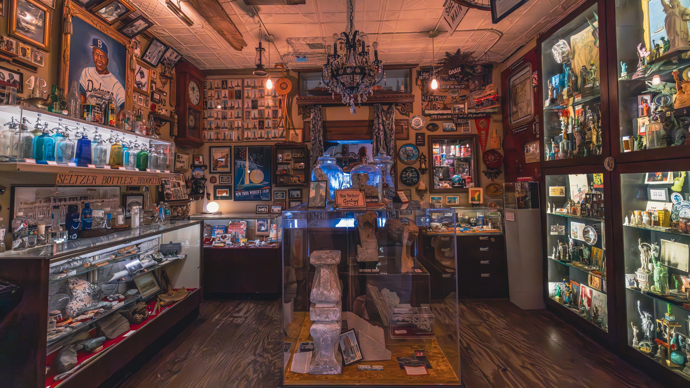A cluttered room filled with vintage memorabilia, bottles, photos, and display cases, warmly lit with eclectic decor.